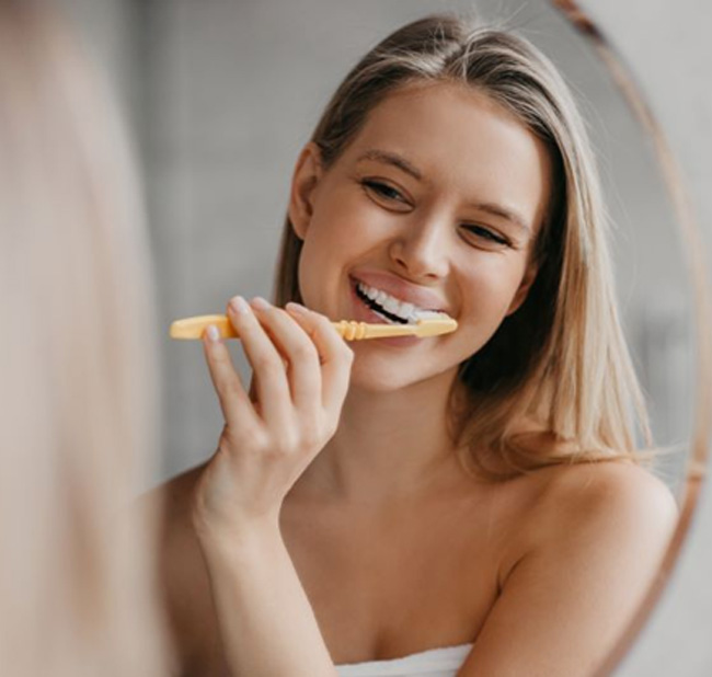 Young woman brushing her teeth in front of mirror